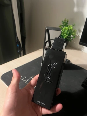 YSL MYSLF Eau de Parfum - Säljer en YSL MYSLF Eau de Parfum i en stilren, svart rektangulär flaska med YSL-loggan i relief på framsidan. Flaskan har en modern design och kommer med originalkartong. Perfekt för dig som gillar exklusiva dofter och snygg förpackning.