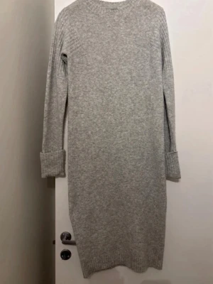 Grå stickad klänning från ASOS - Mysig grå stickad klänning från ASOS med lång ärm och ribbade muddar. Perfekt för kyligare dagar och enkel att styla med boots eller sneakers. Rak passform och mjukt material som känns skönt mot huden.