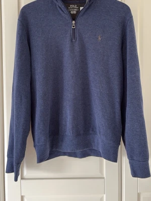 Blå halvzip tröja från Polo Ralph Lauren - Mörkblå långärmad tröja från Polo Ralph Lauren med halv dragkedja och broderad logga på bröstet. Tillverkad i mjukt bomullsmaterial och har ribbade muddar vid ärmslut och nederkant. Perfekt för en avslappnad men snygg stil.