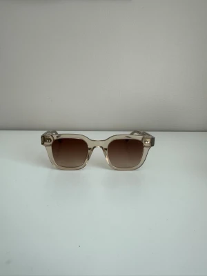 Chimi 04 Ecru - Snygga solglasögon från Chimi med transparent beige båge och fyrkantig form. Glasen är bruna med en lätt toning. Perfekta för att lyfta din stil under soliga dagar. Inga defekter 