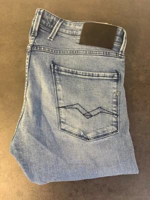 Ljusblå slim fit jeans från Replay stl 33/36 - Snygga ljusblå jeans från Replay i slim fit-modell. Jeansen har klassisk femficksdesign, diskret tvätt och raka ben. Materialet är mjuk denim med stretch för extra komfort. Perfekta för en avslappnad och trendig look.