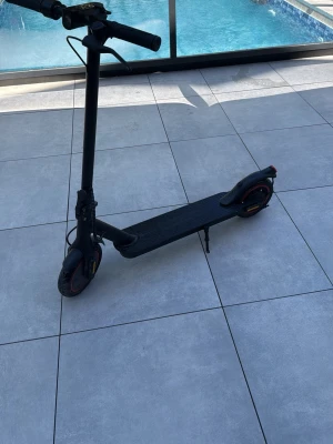 Svart elsparkcykel med röda detaljer - Säljer en svart elsparkcykel med röda detaljer på hjulen och baklyse. Den har en bred fotplatta, handtag med bra grepp och stödben. Perfekt för att ta sig runt i stan på ett smidigt och miljövänligt sätt. Den kan köra 30km i timmen och kan åka 30km range