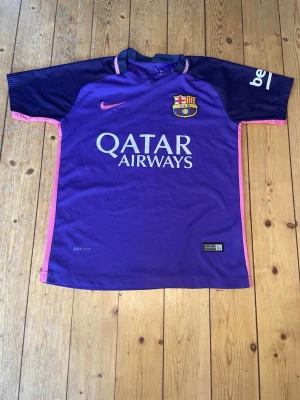 Lila FC Barcelona matchtröja Nike - Snygg lila FC Barcelona matchtröja från Nike med Qatar Airways-tryck på bröstet och klubbmärke. Tröjan har mörkblå ärmar, rosa detaljer längs sidorna och är tillverkad i Dri-FIT material som andas. Perfekt för fotbollsträning eller att bära till vardags. Tröjan passar barn mellan 148-142 cm ca. Priset är inte hugget i sten.
