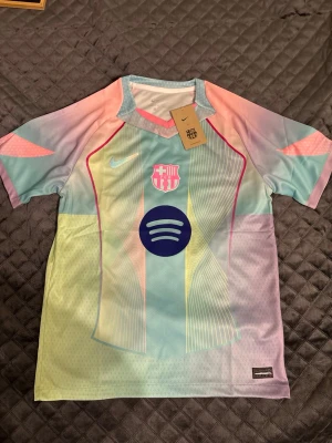 Nike x FC Barcelona pastell matchtröja - Säljer en unik FC Barcelona matchtröja från Nike i pastellfärger med inslag av ljusblått, rosa och gult. Tröjan har klubbmärke, Nike-logga och Spotify som sponsor på bröstet. Tillverkad i lätt, ventilerande Dri-FIT-material. Perfekt för dig som älskar fotboll och streetwear.