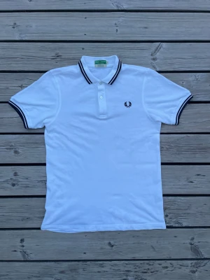 Pikè från Fred Perry - Klassisk vit pikétröja från Fred Perry med marinblå detaljer på krage och ärmslut. Tröjan har korta ärmar, knappar framtill och den ikoniska Fred perry logan! Fråga vid fundering, pris kan ändras vid snabbt köp!😃😃