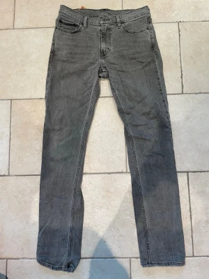 Grå raka jeans från Levi's 511 - Säljer ett par grå jeans från Levi's med klassisk femficksdesign och raka ben. Jeansen har en diskret tvättad look och är tillverkade i bomull. Passar perfekt till en avslappnad stil och har den ikoniska röda Levi's-lappen på bakfickan. Storlek är W30 och L34 och modell är 511
