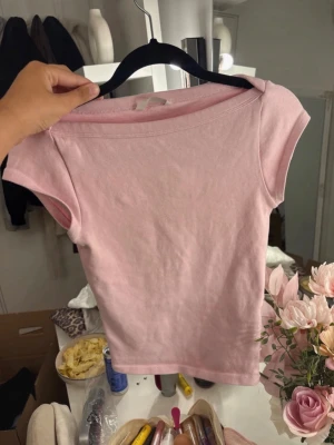 Ljusrosa kortärmad topp - Söt ljusrosa topp i mjuk bomull med enkel och stilren design. Modellen är figurnära med korta ärmar och rund halsringning. Perfekt att matcha med jeans eller kjol för en avslappnad look.