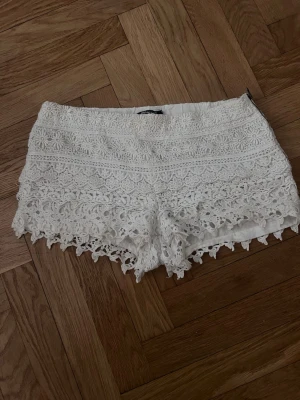 Vita spets-shorts från Gina Tricot - Supersnygga vita shorts från Gina Tricot med detaljerad spets och volangkant. De har en feminin look och är perfekta för varma dagar. Elastisk midja för skön passform och tunnt innerfoder💕