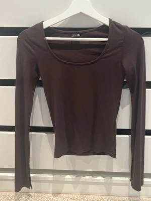 Mörkbrun långärmad topp Gina Tricot - Säljer en mörkbrun långärmad topp från Gina Tricot. Toppen har en rund, djup ringning och är i ett mjukt, stretchigt material som sitter tight mot kroppen. Perfekt att styla med jeans eller kjol för en enkel och snygg look.