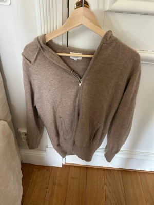 Beige cashmere hoodie Soft Goat - Mysig beige hoodie i 100% kashmir från Soft Goat. Tröjan har dragkedja framtill, två fickor och huva. Perfekt för dig som gillar en avslappnad men ändå stilren look. Superskön och lyxig känsla tack vare det mjuka materialet.