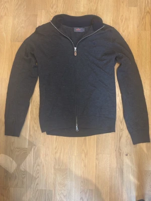 Brun ziptröja från Morris - Snygg brun ziptröja från Morris med mörkblå krage och hel dragkedja. Tröjan har diskret broderad logga på bröstet och ribbade muddar vid krage och ärmslut. Tillverkad i mjukt material som känns skönt mot huden. Perfekt för en stilren och avslappnad look.