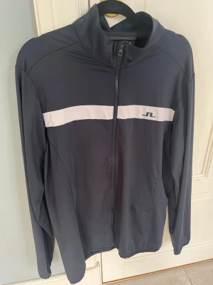 Mörkblå ziptröja från J.Lindeberg - Sportig mörkblå ziptröja från J.Lindeberg. Funkar till både golf och att ha i vardagen. Perfekt för en avslappnad och stilren look.