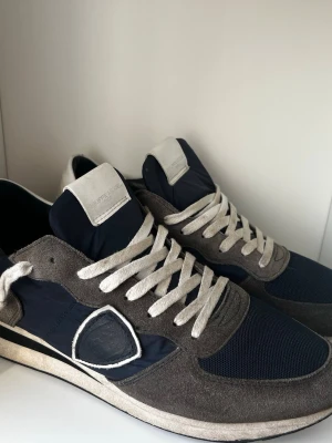 Philippe Model blå/grå sneakers - Pris kan diskuteras✅Snygga sneakers från Philippe Model i marinblått och grått med vita detaljer. Ovandelen är i mocka och mesh, med vita skosnören och logga på sidan.  Två små skråmor, syns inte alls vid användning.
