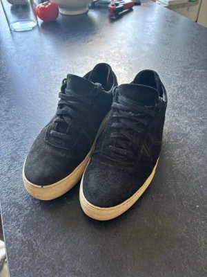 Svarta sneakers i mocka - Stilrena svarta sneakers i mocka med svart snörning och vit, tjock sula. Klassisk låg modell som passar till det mesta och ger en clean look. Perfekta för dig som gillar enkel och tidlös stil.