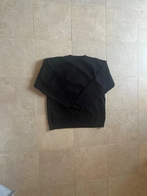 Svart stickad tröja med rött hjärta - Säljer en svart stickad tröja med ett stort rött hjärta och bokstaven A på bröstet. Tröjan har rund halsringning, långa ärmar och ribbade muddar. Perfekt för dig som gillar enkel men snygg design.