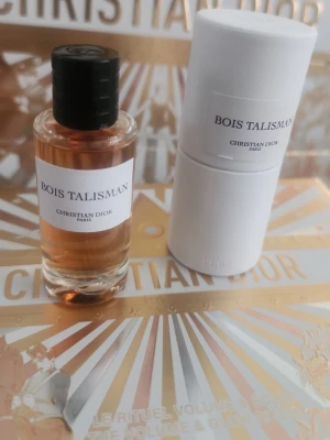 Bois Talisman parfym från Dior 10 ml - Bois Talisman från Christian Dior är en exklusiv parfym i en rund glasflaska med svart kork och vit etikett. Doftvätskan har en varm bärnstensfärg och flaskan kommer med en elegant vit cylinderformad förpackning. Perfekt för dig som gillar lyxiga och stilrena dofter.