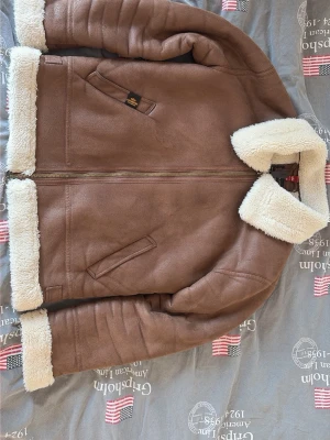 Brun pilotkappa med fuskpäls - Snygg brun pilot jacka från alpha industries med mjuk päls inuti. Jackan har dragkedja, två snedställda fickor och bred krage. Perfekt för kalla dagar och ger en klassisk vintage-look. Perfekt under vinter har aldrig frusit i denna. 