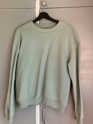 Ljusgrön sweatshirt från 157 - En stilren ljusgrön sweatshirt från 157 med rund halsringning och ribbade muddar vid ärmslut och nederkant. Tröjan har en avslappnad passform och är tillverkad i mjukt material som passar perfekt till jeans eller mjukisbyxor.