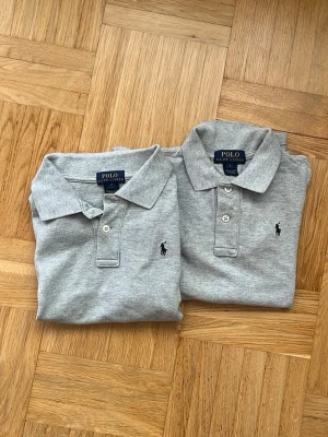  2 Grå pikétröjor från Polo Ralph Lauren - Två stilrena grå pikétröjor från Polo Ralph Lauren med klassisk krage, knappslå och broderad logga på bröstet. Tröjorna är kortärmade och tillverkade i mjuk bomull för en bekväm känsla. Perfekt för en clean och avslappnad look. Perfekt till skolavslutningen i sommar!🌸😊 2st 600kr 1st 250kr