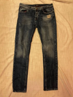 Philipp Plein blå slitna jeans - Snygga blå jeans från Philipp Plein med slitningar och patchdetalj framtill. Jeansen har smal passform och klassisk femficksdesign. Perfekta för en trendig och avslappnad look. W31 L30 tror jag