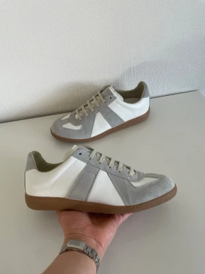 Vita och grå gats från masion margiela - Snygga vitt och ljusgrått gats från masion margiela med ovandel i mocka och läder. Klassisk låg modell med beige snörning och bruna gummisulor. Perfekta för en clean och stilren look. Inspirerade av retrodesign och passar till det mesta.