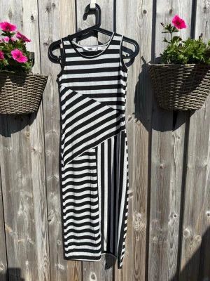 Randig svartgrå klänning - Snygg svartgrå klänning med olika breda ränder i både horisontella och diagonala mönster. Ärmlös modell med rund halsringning och mjukt, stretchigt material som känns bekvämt. Perfekt för dig som gillar grafiska mönster och en cool look.