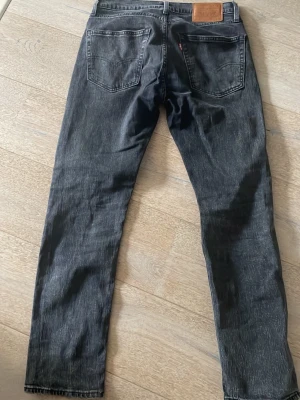 Mörkgrå Levi's jeans - Säljer ett par svarta jeans från Levi's med klassisk femficksdesign och raka ben. Jeansen har en läderpatch bak i midjan och subtila sömmar. Perfekta för dig som gillar en enkel och tidlös look. Modell 502.