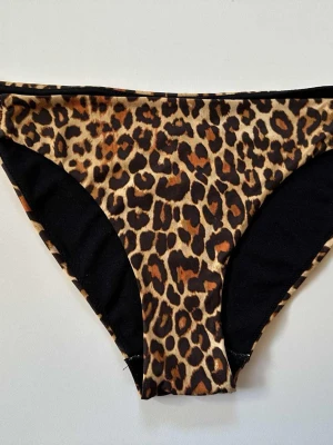 Bikinitrosor strl 42 leopard - Snygg bikiniunderdel med leopardmönster i bruna och svarta toner. Klassisk trosa-modell med bekväm passform, perfekt för strand eller pool. Materialet är mjukt och följsamt syntetiskt tyg som torkar snabbt.