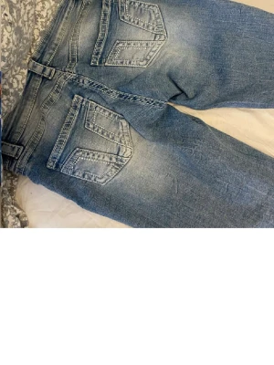 Bootcut ljusblå jeans med slitningar - Säljer ett par ljusblå bootcut jeans med snygga slitningar och markerade sömmar. Jeansen har klassiska fem fickor och en låg midja. Perfekta för dig som gillar en avslappnad och trendig stil.