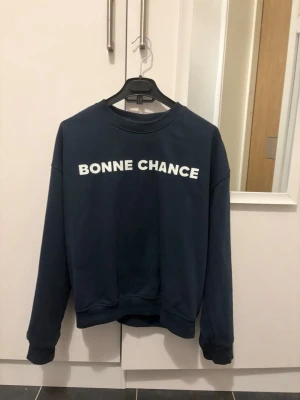 Mörkblå sweatshirt med tryck - Mörkblå sweatshirt med vit text 'BONNE CHANCE' framtill. Klassisk rund halsringning och långa ärmar. Mjuk och bekväm modell i bomullsmix, perfekt för en avslappnad stil.