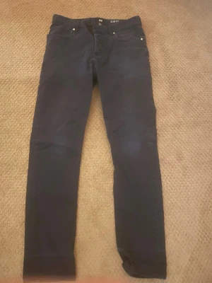 Svarta slim fit jeans från H&M - Säljer ett par svarta slim fit jeans från H&M med klassisk femficksdesign och smal passform. Jeansen har normal midja och är tillverkade i ett stretchigt material för extra komfort. Perfekta till en avslappnad stil.