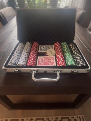 Poker set i aluminiumväska - Säljer ett komplett poker set i en silverfärgad aluminiumväska. Innehåller pokermarker i vitt, blått, rött, grönt och svart, två kortlekar och en dealer-bricka. Perfekt för pokerkvällar med vänner. Väskan har skumfoder på insidan för skydd.
