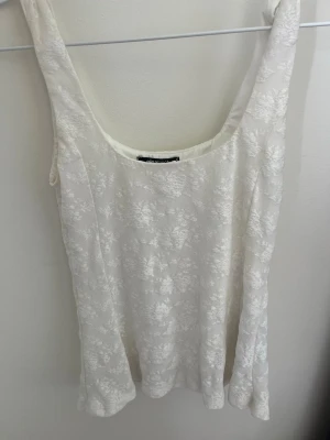 Vit blommig spetslinnetopp - Säljer en söt vit linnetopp från Gina Tricot med blommigt spetsmönster. Toppen är ärmlös och har en rundad urringning. 