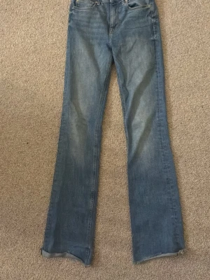 Blå bootcut jeans från ZARA - Snygga blå bootcut jeans från ZARA med klassisk femficksdesign och normalhög midja. Jeansen har en lätt tvättad look och är tillverkade i denim. Perfekta för dig som gillar en avslappnad men trendig stil.