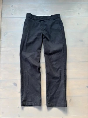 Dickies 874, strl 31 - Säljer ett par klassiska svarta chinos från Dickies. Byxorna har raka ben, bälteshällor och två fickor fram samt två bakfickor. Materialet är slitstarkt och har en matt finish. Perfekta för en clean och enkel stil.