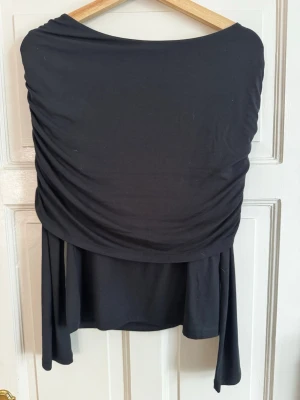Svart draperad topp från Bubbleroom - Svart topp från Bubbleroom med snygg drapering. Toppen är tillverkad i ett mjukt, stretchigt material som känns skönt mot huden. Perfekt för dig som gillar en stilren och modern look. Aldrig använd och prislapp sitter kvar.💕