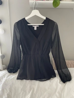 Svart blus  - V-ringad svart blus. Blusen har puffärm och är insyd runt midjan. I storlek 36 från Nelly 
