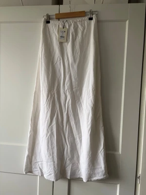 Vit lång kjol från Gina Tricot - Säljer en vit lång kjol från Gina Tricot i linnemix. Kjolen har elastisk midja och ett luftigt, rakt fall som ger en clean och fräsch look. Perfekt till sommaren och enkel att styla med olika toppar.