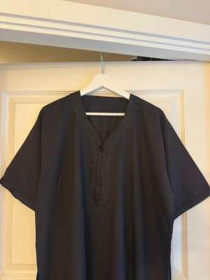 Svart marockansk thobe, oanvänd - Storlek 56. Passar för dig med en längd på ungefär 175-180cm. Kommer i sluten förpackning.