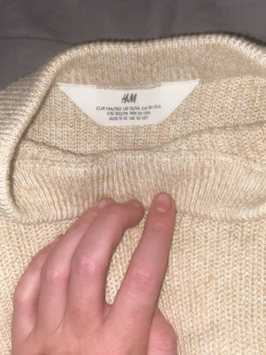 Beige stickad tröja från H&M - Stickad tröja i mjuk beige färg från H&M. Tröjan har rund halsringning och ribbade muddar vid hals, ärmslut och nederkant. Enkel och stilren design som passar perfekt till många olika outfits.