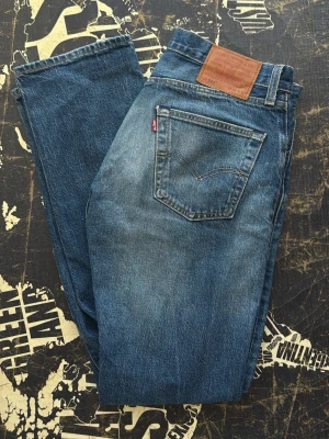 Levi's 501 blå raka jeans - Klassiska blå Levi's 501 jeans med rak passform och femficksdesign. Jeansen har en vintagekänsla med snygg tvätt och läderpatch bak i midjan. Tillverkade i slitstark bomullsdenim och har den ikoniska röda Levi's-taggen på bakfickan.