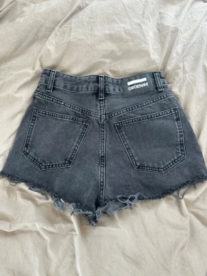 Svarta jeansshorts från Dr Denim - Säljer ett par svarta jeansshorts från Dr Denim med hög midja och råa, fransiga benslut. Shortsen har två bakfickor och bälteshällor. 
