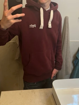 Superdry hoodie - Säljer denna riktigt feta superdry hoodien i storlek S. Den är i gott skick och är i en riktigt snygg vinröd färg. Killen på bilden är 177cm. Priset är ej hugget i sten och det är bara höra av sig vid frågor!