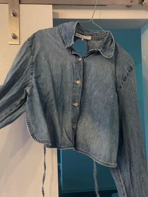 Cropped jeanströja  från Zara - Snygg ljusblå cropped jeanströja från Zara med klassisk krage och knappar framtill. Tröjan har långa ärmar och en avslappnad passform som ger en cool vibe. Perfekt att slänga över en t-shirt för en trendig look.