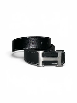 Svart skärp med H-spänne - Stilrent svart skärp från i skinn med ett ikoniskt H-format metallspänne. Skärpet har vita kontrastsömmar längs kanterna som ger en snygg detalj. Perfekt accessoar för att lyfta din outfit.