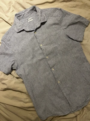 Randig skjorta från Zara i bomull - Säljer en snygg vit och blå randig skjorta från Zara med regular fit. Skjortan har klassisk krage, knappar framtill och är tillverkad i mjuk bomull. Perfekt för en clean och avslappnad stil. Säljer den eftersom den tyvärr inte passar längre. Använts 3 gånger.