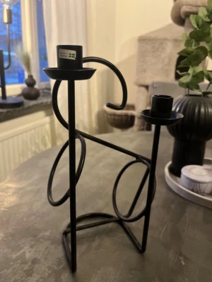 Svart ljusstake i metall, Made in Sweden - Unik svart ljusstake i metall med modern, geometrisk design och plats för två ljus samt en vinhållare. Märkt med 'Made in Sweden'. Perfekt som snygg inredningsdetalj på bord eller hylla. 