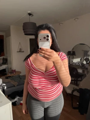 Rödvit randig croppad topp - Säljer en röd och vit randig croppad topp med v-ringning och korta ärmar. Toppen har en figurnära passform och är tillverkad i ett mjukt, stretchigt material som känns bekvämt mot huden. Perfekt för dig som gillar en enkel men snygg stil.