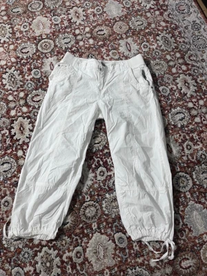 Vita mjukisbyxor med dragsko - Säljer ett par vita mjukisbyxor med resår i midjan och dragsko vid bensluten. Byxorna har fickor fram och bak, samt en avslappnad passform. Perfekta för en chill och bekväm stil.