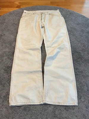 Beiga vida jeans från Wrangler - Säljer ett par beiga jeans från Wrangler med raka, vida ben och klassiska bakfickor med W-detalj. 